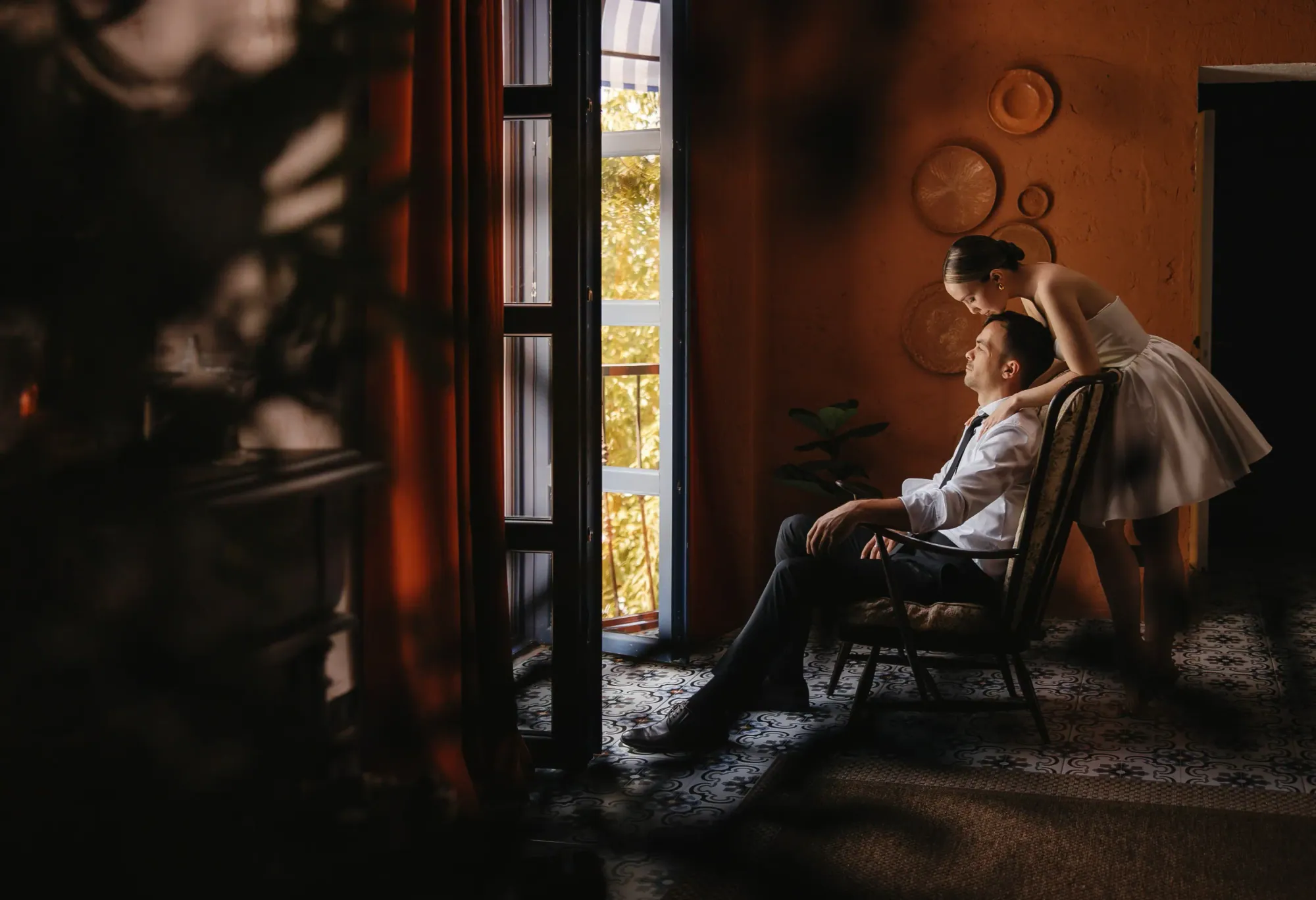 Cuplu lângă fereastra înaltă, într-un salon cu pereți teracotă