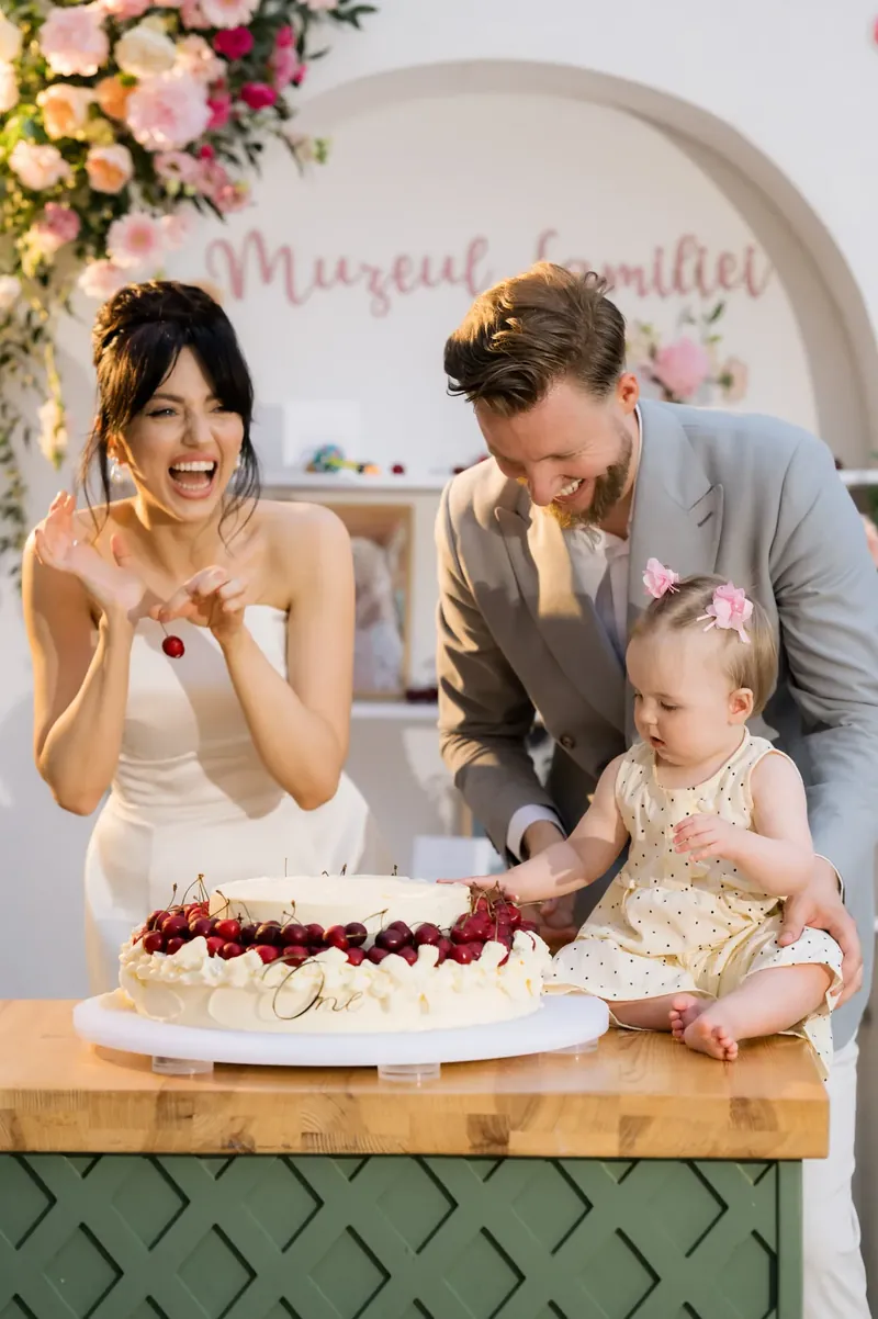 Familie cu bebeluș lângă tortul aniversar decorat cu cireșe